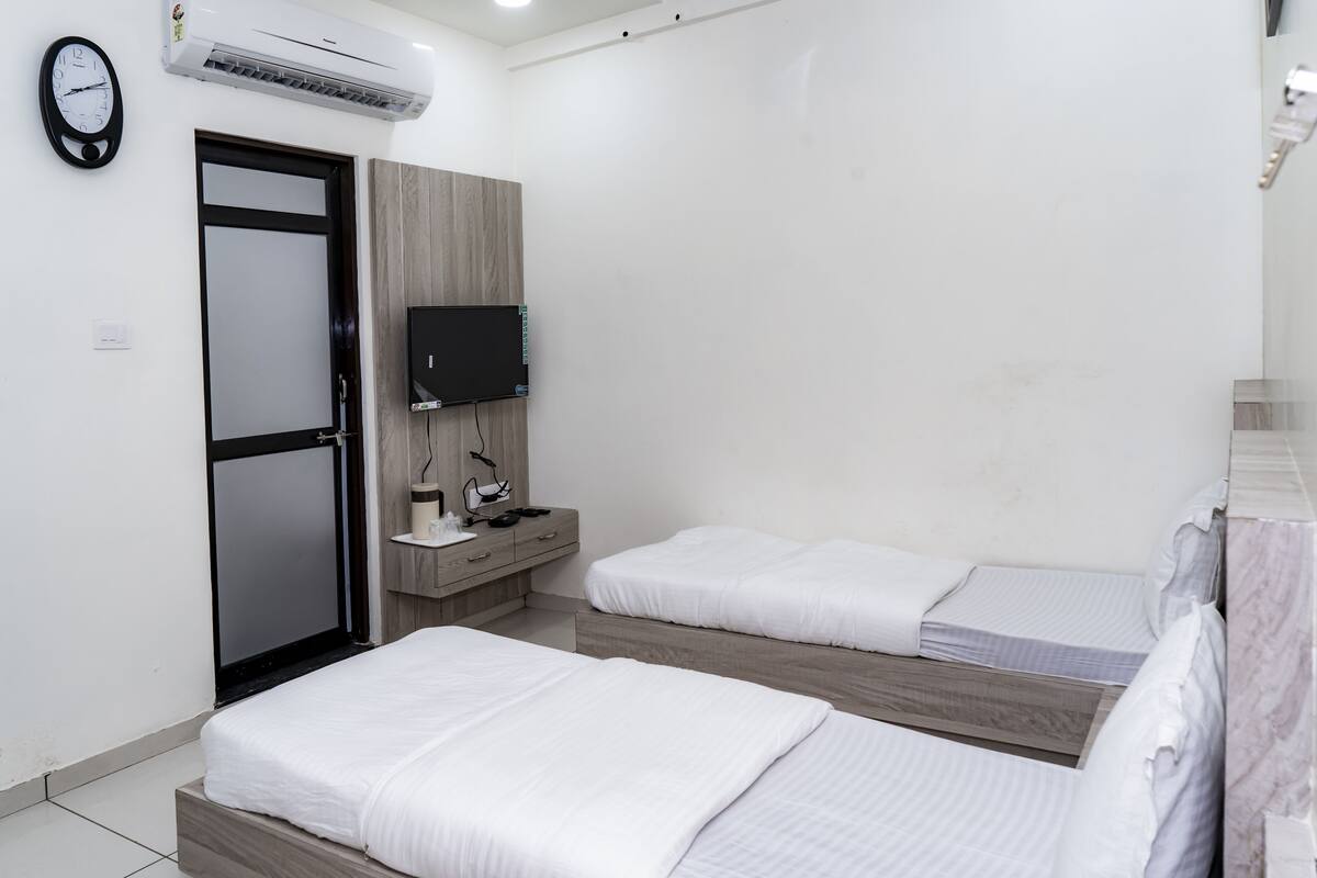 A hotel room with two beds, a TV, a desk with a chair, and a door.
