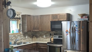 A kitchen with wooden cabinets, a stainless steel refrigerator, a microwave, and an island with a sink. - Beautiful house on the Paradise Eckerman boarder. (Eckerman)