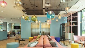 A modern lounge area with a pink sofa, blue and yellow ottomans, and a variety of hanging pendant lights. - Holiday Inn - the niu, Belt Frankfurt Eschborn by IHG (Eschborn)