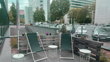 Una terraza en la azotea con sillas verdes y una pequeña mesa, rodeada por una valla de metal.