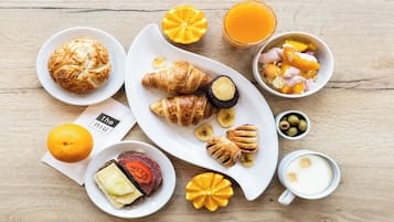 A breakfast setting with croissants, a sandwich, fruit, and a glass of orange juice on a wooden table.