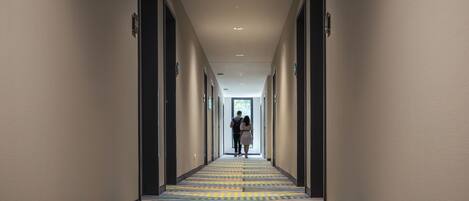 Pasillo de hotel con alfombra estampada, puertas a ambos lados y vista a una habitación al final.
