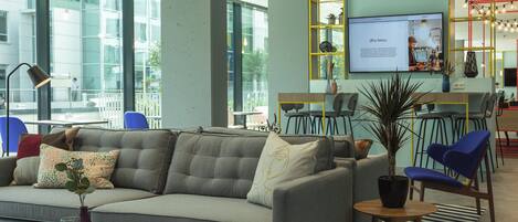A modern lounge area with a sofa, round tables, and blue chairs.