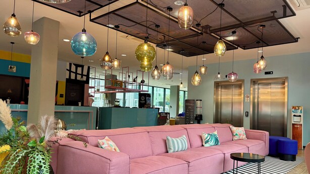 A modern lounge area with a pink sofa, hanging pendant lights, and a striped floor. - Holiday Inn - the niu, Belt Frankfurt Eschborn by IHG (Eschborn)
