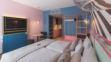 A modern hotel room with a bed, a small table, a chair, a TV, and a kitchenette.