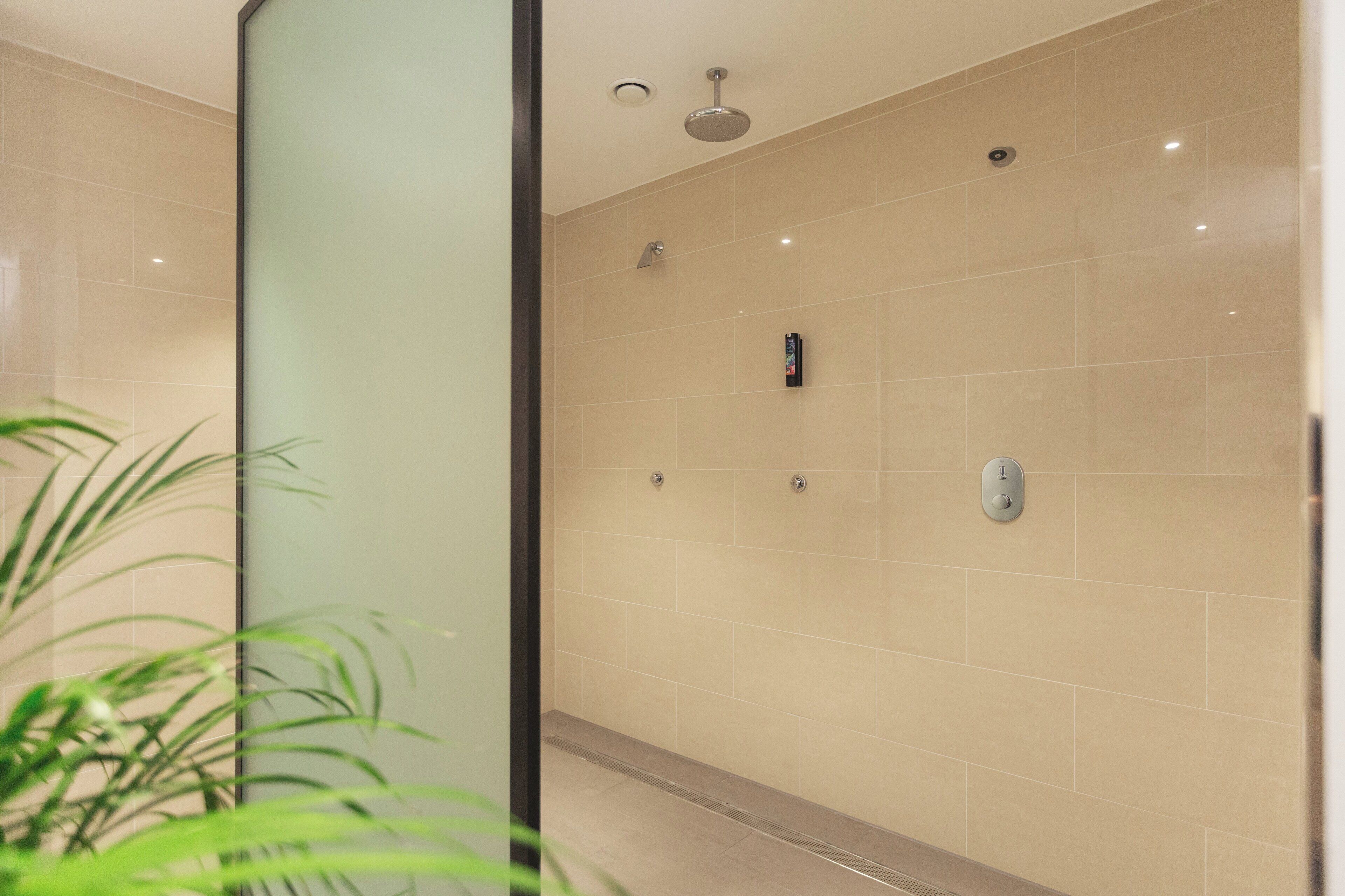 Un baño moderno con azulejos color beige, una cabina de ducha de vidrio y un panel de control visible.