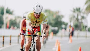 A cyclist in a yellow and green outfit riding a bicycle on a road with orange traffic cones.