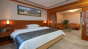 Ein Hotelzimmer mit einem großen Bett, einem Holzkopfende, einem Nachttisch, einem Schreibtisch, einem Sessel und einer Tür zu einem anderen Raum.