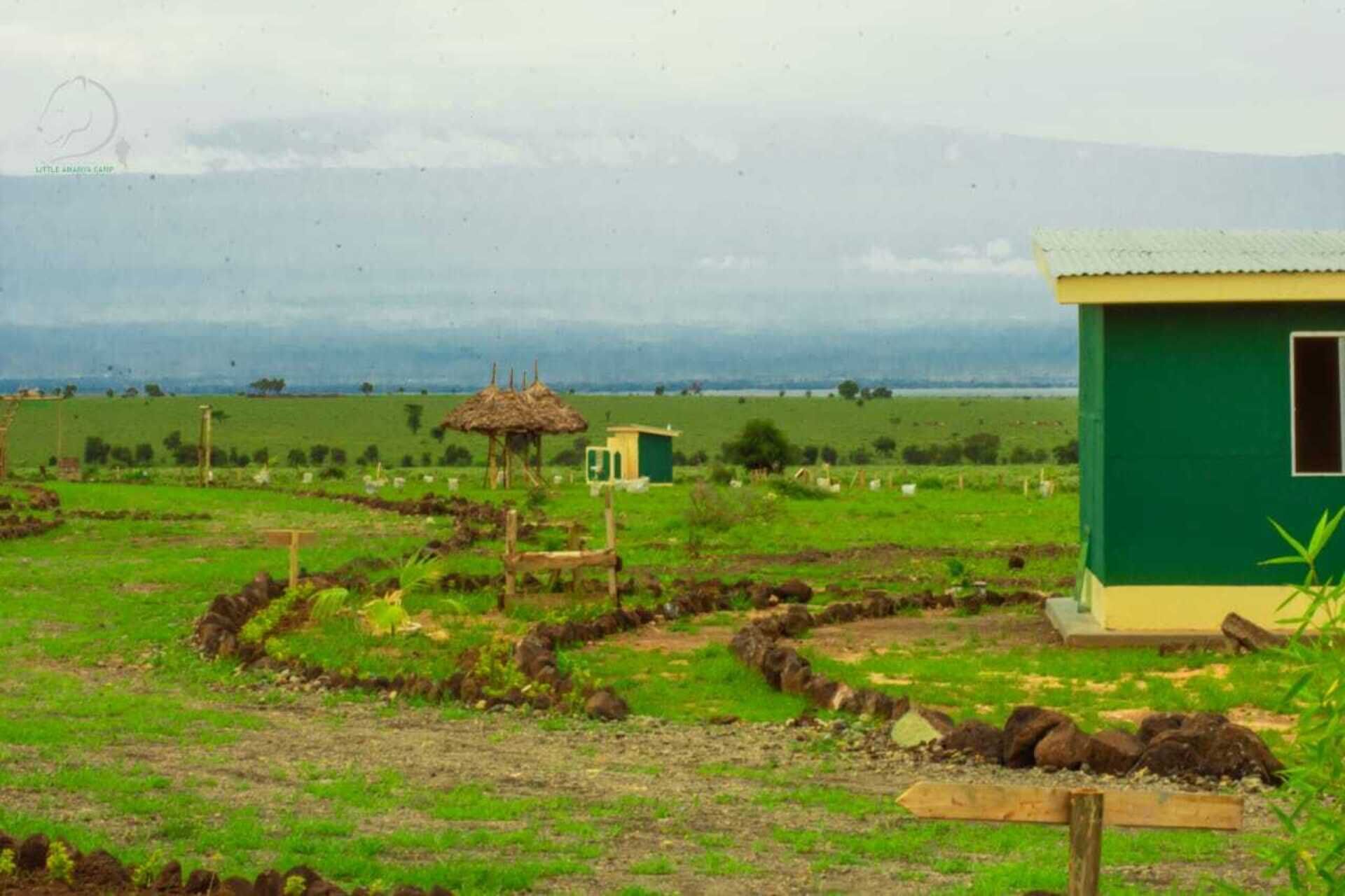 Paisaje rural con un edificio verde, una estructura de paja y una zona cercada.