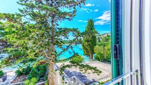 Vista desde una ventana con vista a una zona costera, árboles y mar azul cristalino.