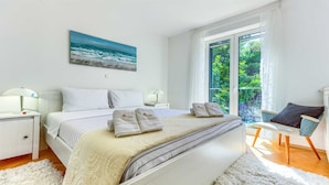 Un dormitorio con cama, dos mesitas de noche, una silla, ventana con vistas a la vegetación y un cuadro en la pared.