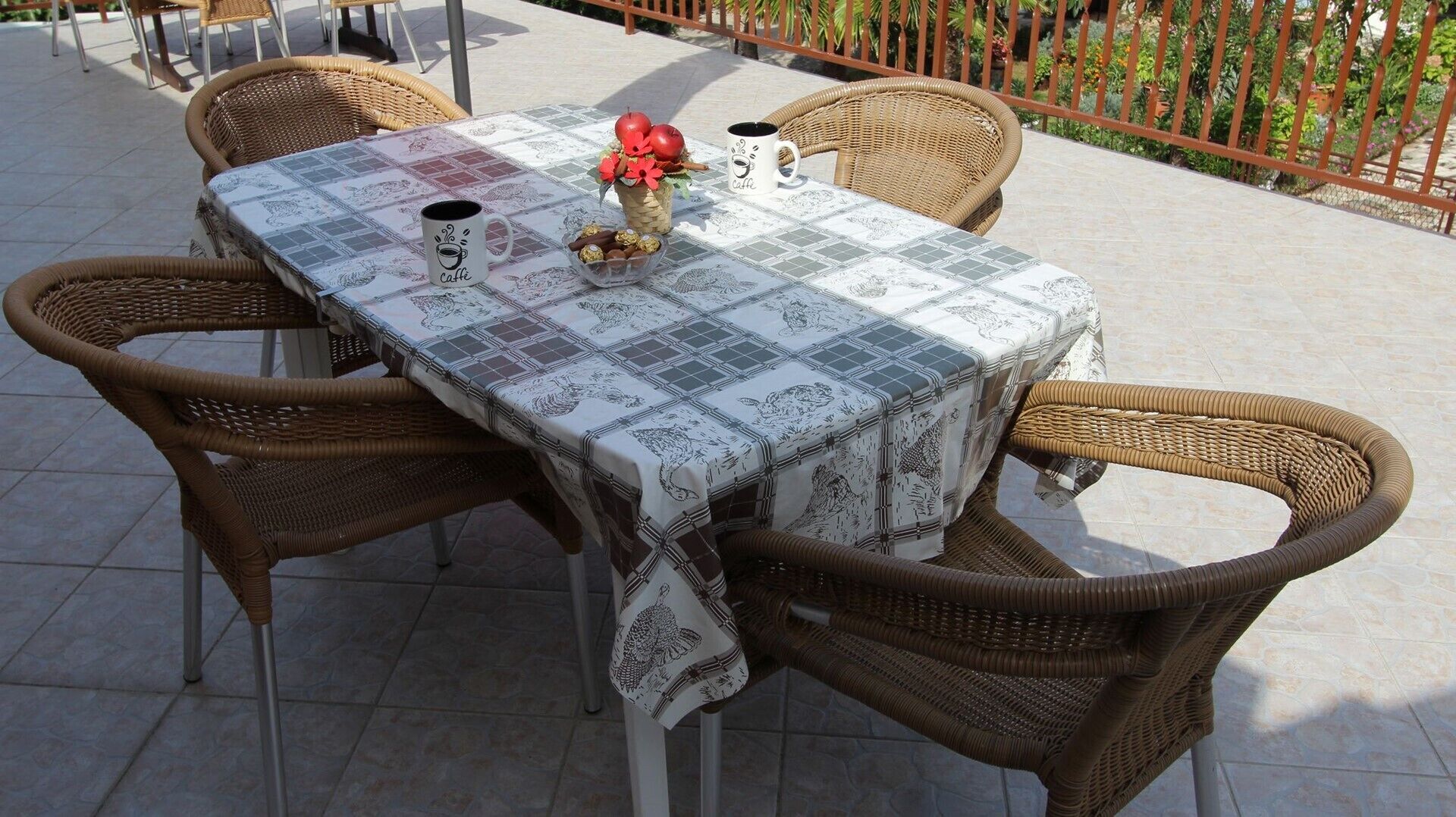 A table set with a tablecloth, two wicker chairs, and a coffee mug.