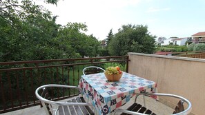 Un balcón con una mesa y sillas, un cuenco de fruta y vistas a zonas verdes y edificios.