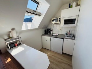 Una cocina compacta con encimera blanca, microondas, cafetera y lavavajillas.