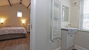 Un dormitorio con cama, lámparas de noche, un radiador, una ventana y un baño con lavabo y espejo.