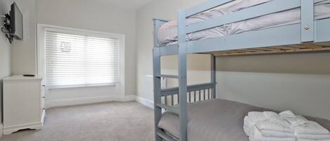 A bunk bed room with a window, a radiator, and a small white cabinet.