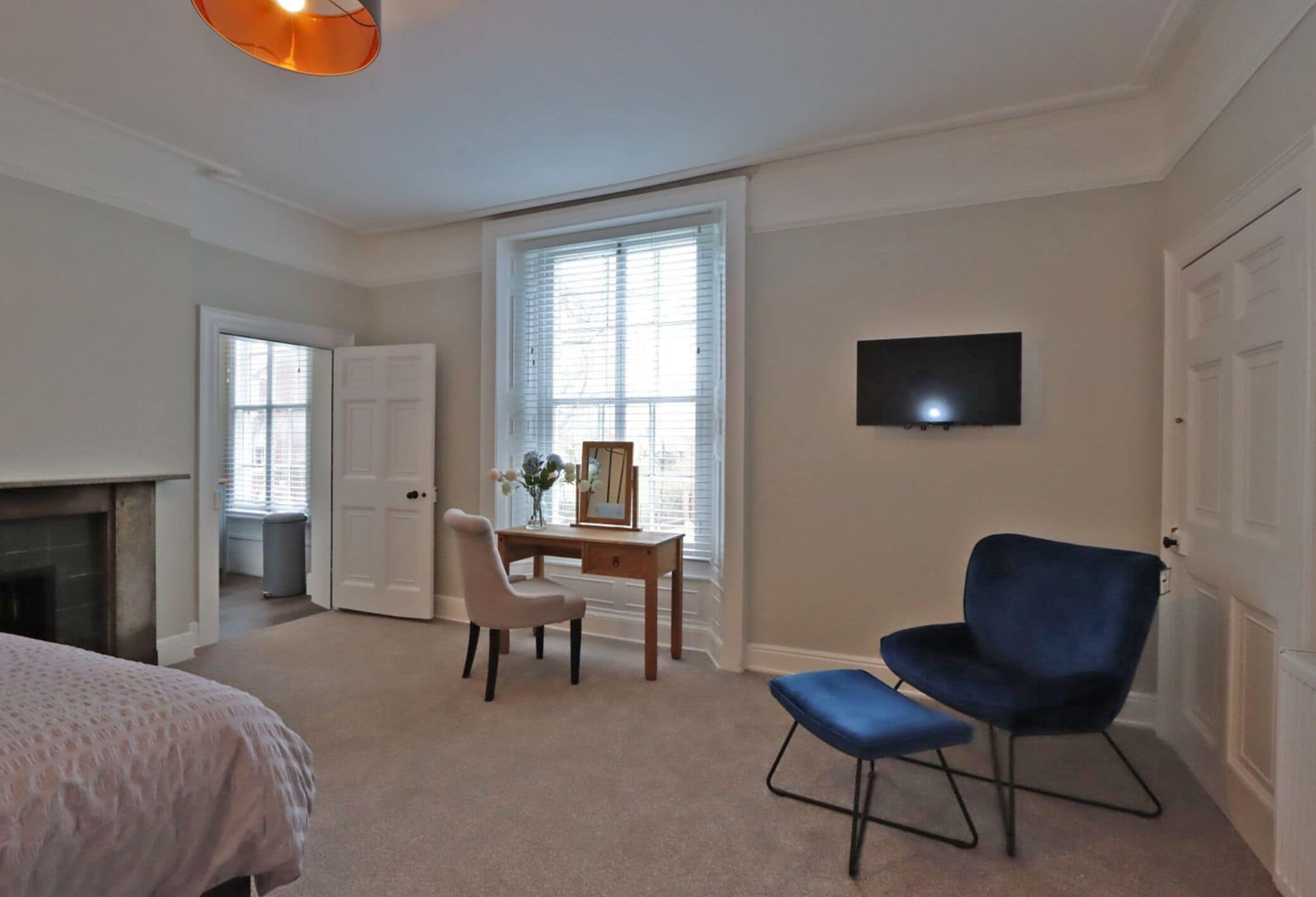 Een slaapkamer met een bed, een bureau met stoel, een televisie en een open haard.