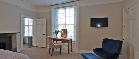 A bedroom with a bed, a desk with a chair, a TV, and a fireplace.