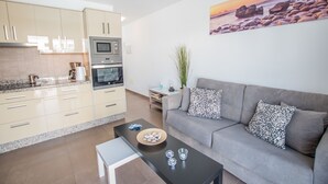 A modern kitchen with a microwave, oven, and granite countertop. There is a grey sofa with patterned cushions and a painting of a beach scene on the wall. - Casa Anemona with terrace, shared pool, sea views and free wifi (Puerto del Carmen)