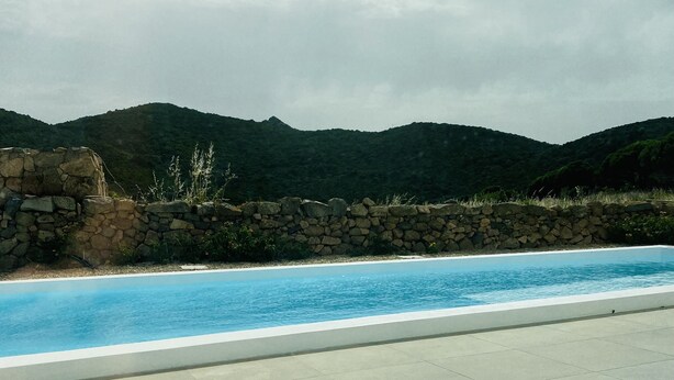 A swimming pool with a stone wall and a view of green hills.