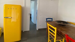 A compact kitchen with a yellow refrigerator, a wooden dining table with blue and red chairs, and a visible door leading to another room.