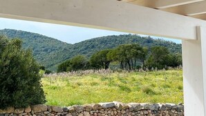 A wooden ceiling structure with a view of a grassy field and trees in the background.