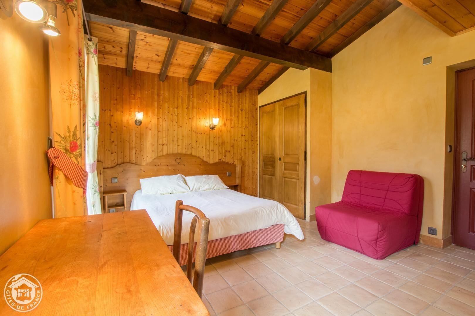 A wooden room with a bed, a red chair, and a wooden table.