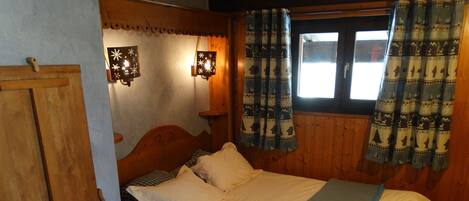 A cozy bedroom with a wooden headboard, a bed with white and blue bedding, two wall-mounted lights, and patterned curtains.