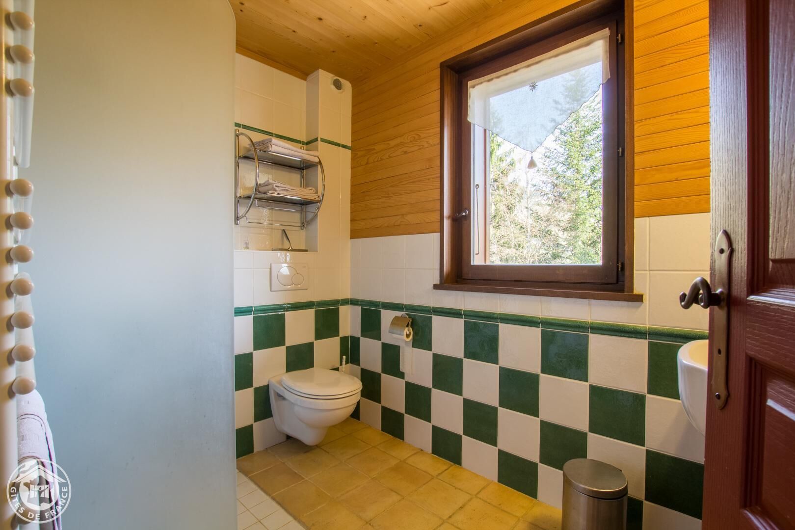 Ein kleines Badezimmer mit Wandbelag aus schwarz-weißen Karos, einer weißen Toilette, einem Fenster und einer Holzboden.