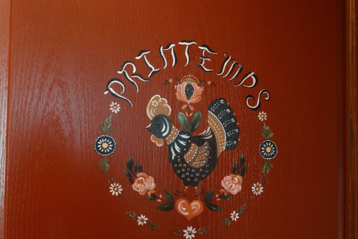 Eine Holztür mit einem dekorativen Wappen, das einen Vogel, Blumen und den Schriftzug "PRINTES & STROKES" zeigt.