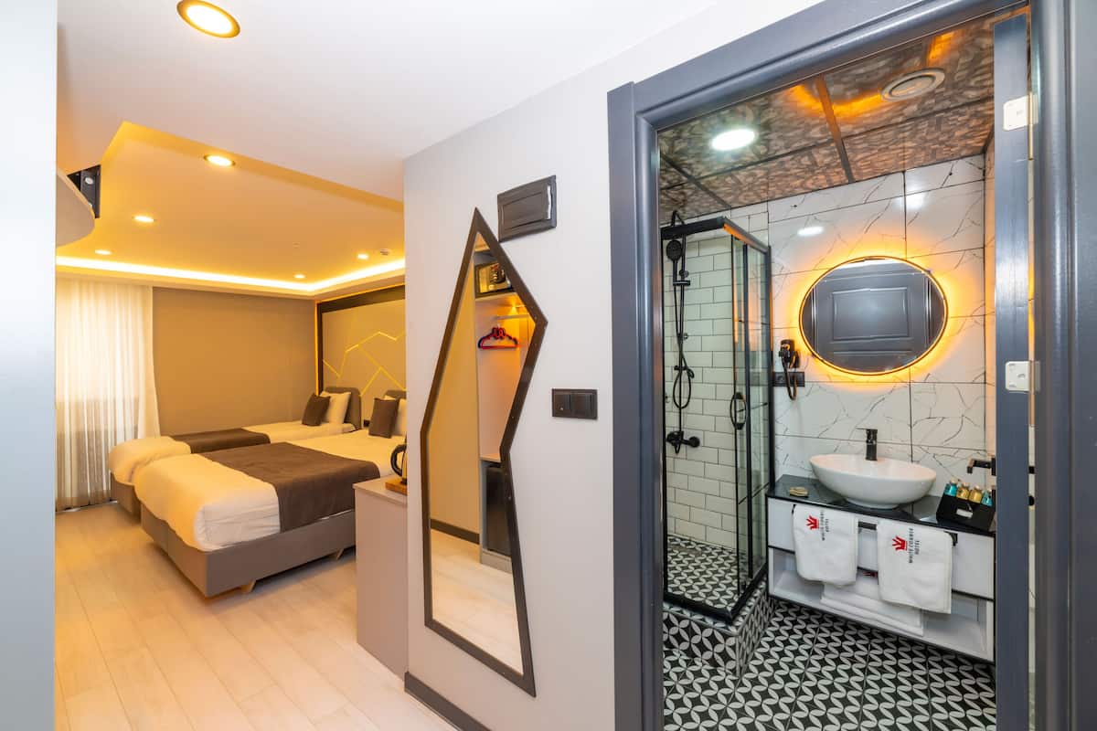 A modern hotel room with a bed, bedside table, and a bathroom with a sink and mirror.