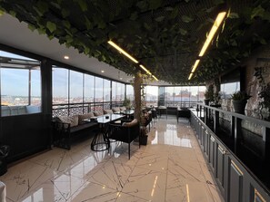 Eine moderne Rooftop-Lounge mit weiter Aussicht auf die Stadt, ausgestattet mit verschiedenen Sitzbereichen und einem Essbereich.