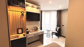 A compact hotel room with a kitchenette, a bed, a small table with a chair, and a large window with curtains.