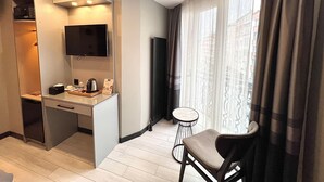 Ett modernt hotellrum med ett litet pentry, en platt-TV, ett litet runt bord och en stol.