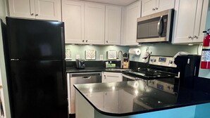 Una cocina moderna con gabinetes blancos, un refrigerador negro, un microondas y una isla grande con taburetes de bar.