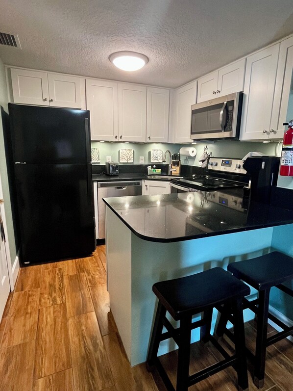 A modern kitchen with white cabinets, a black refrigerator, a microwave, and a large island with bar stools.