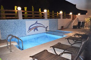 Piscina exterior con un mosaico de delfín, terraza de madera y sillones de descanso.
