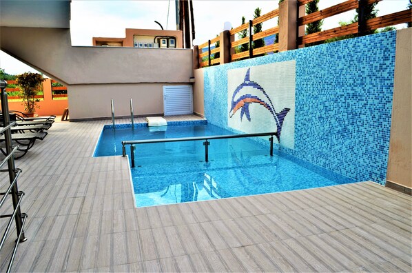 Una piscina con un mosaico de delfín, zona de tumbonas y solárium con baldosas.