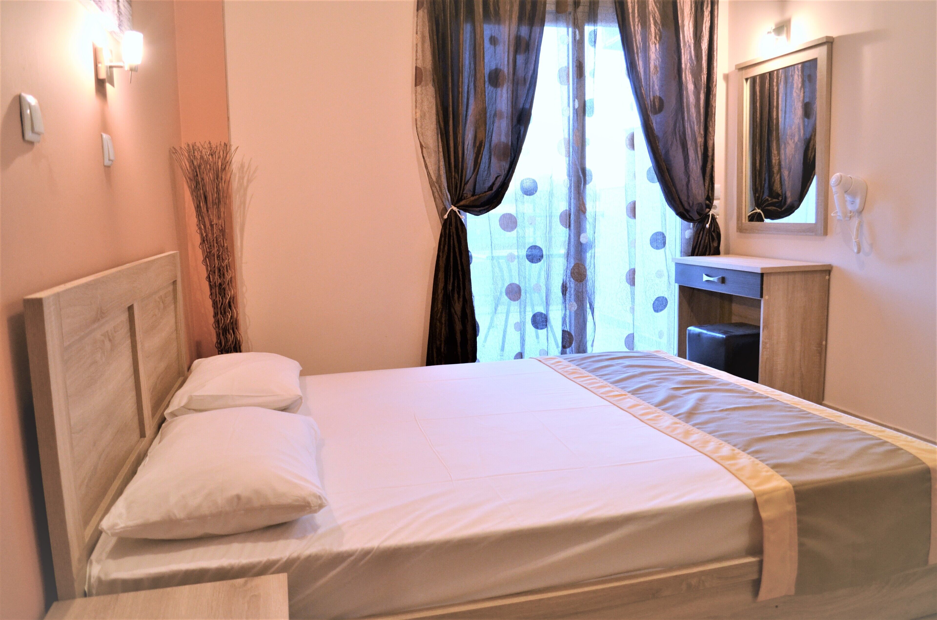 A neatly made bed with a headboard, a bedside table with a lamp, and a mirror above it.