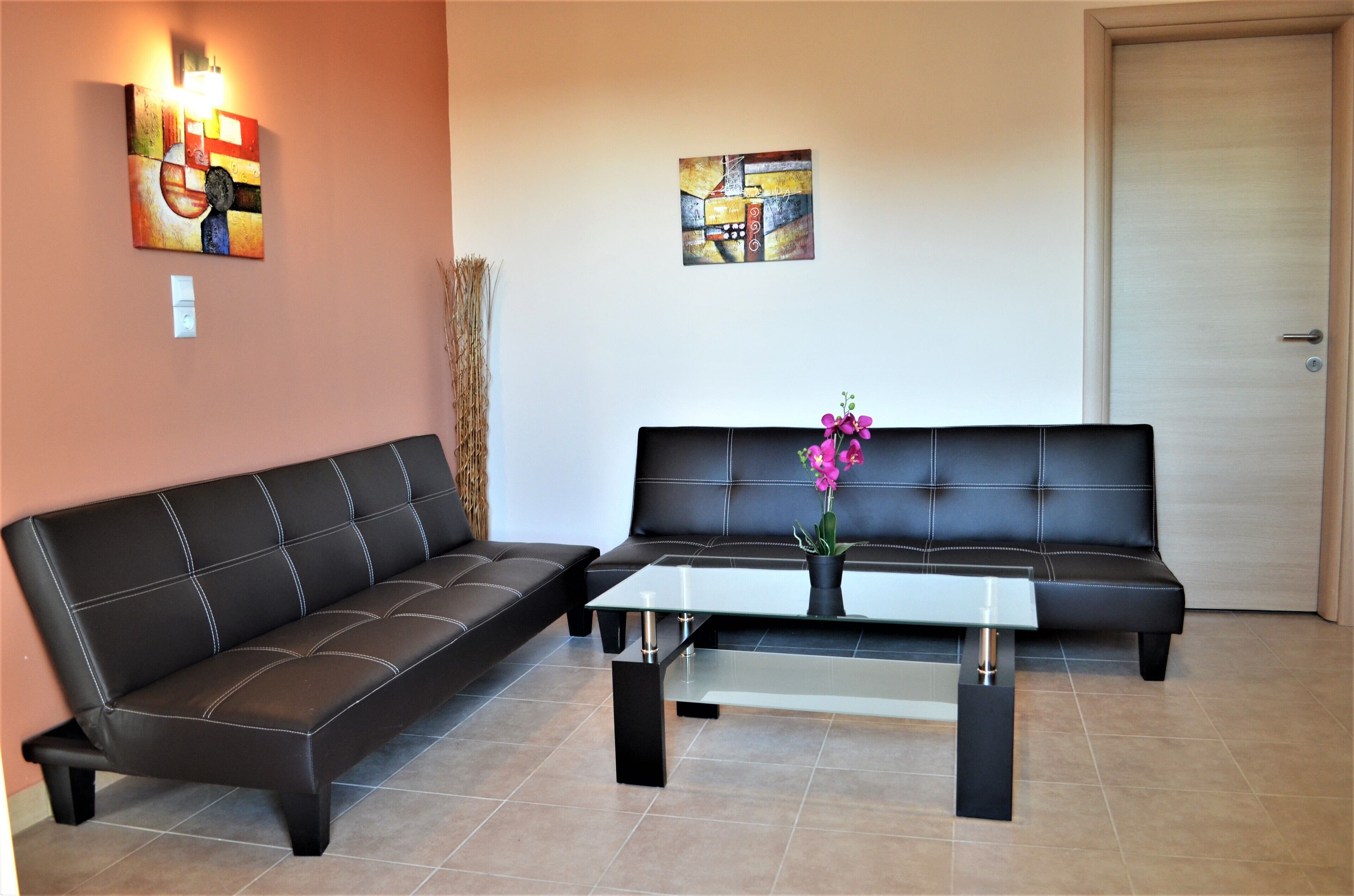 A living room with two black leather sofas, a glass coffee table, and two abstract paintings on the walls.