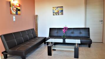 A living room with two black leather sofas, a glass coffee table, and two abstract paintings on the walls.