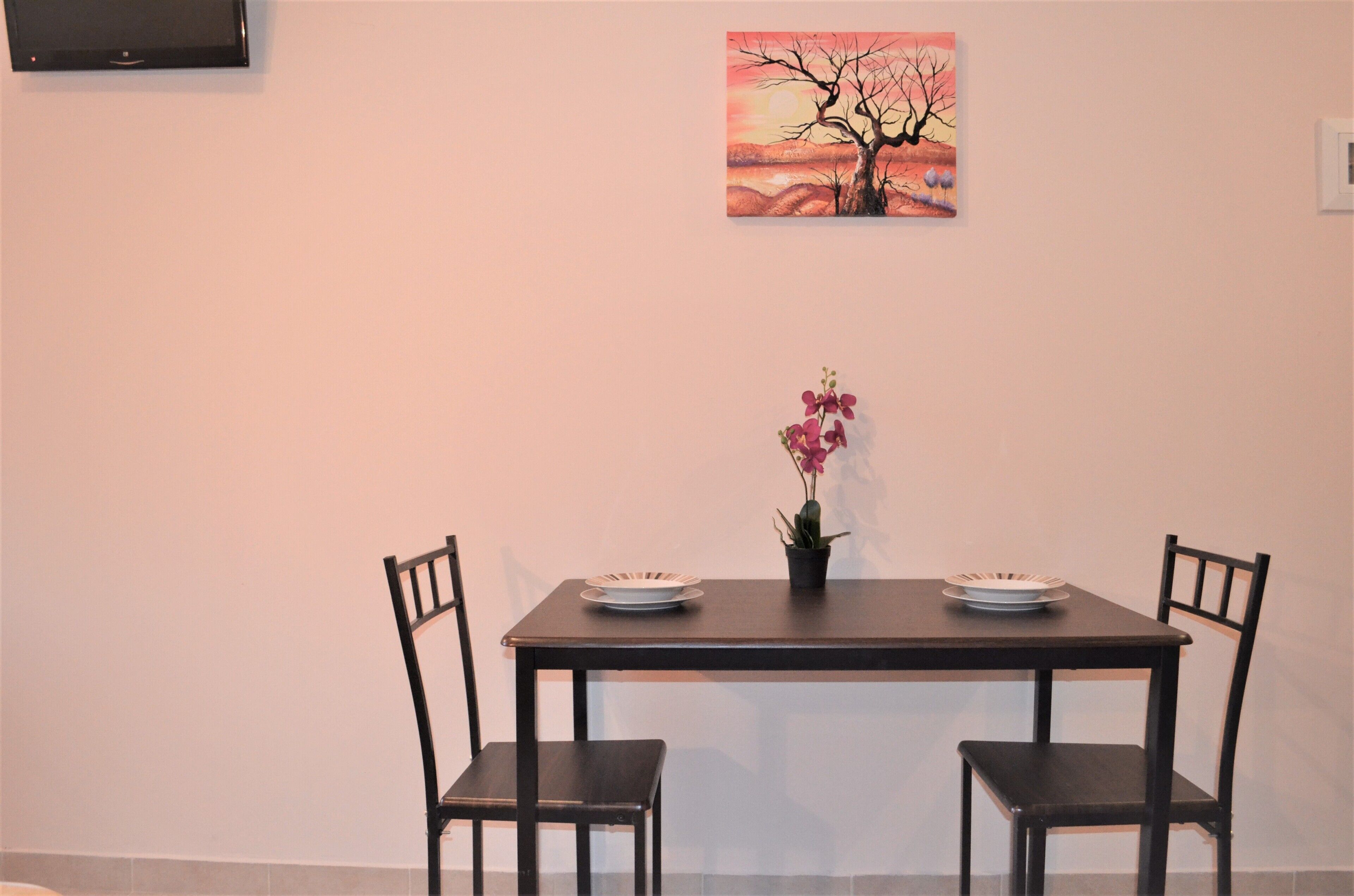 Una mesa de comedor con dos sillas, una planta en maceta y un cuadro en la pared.