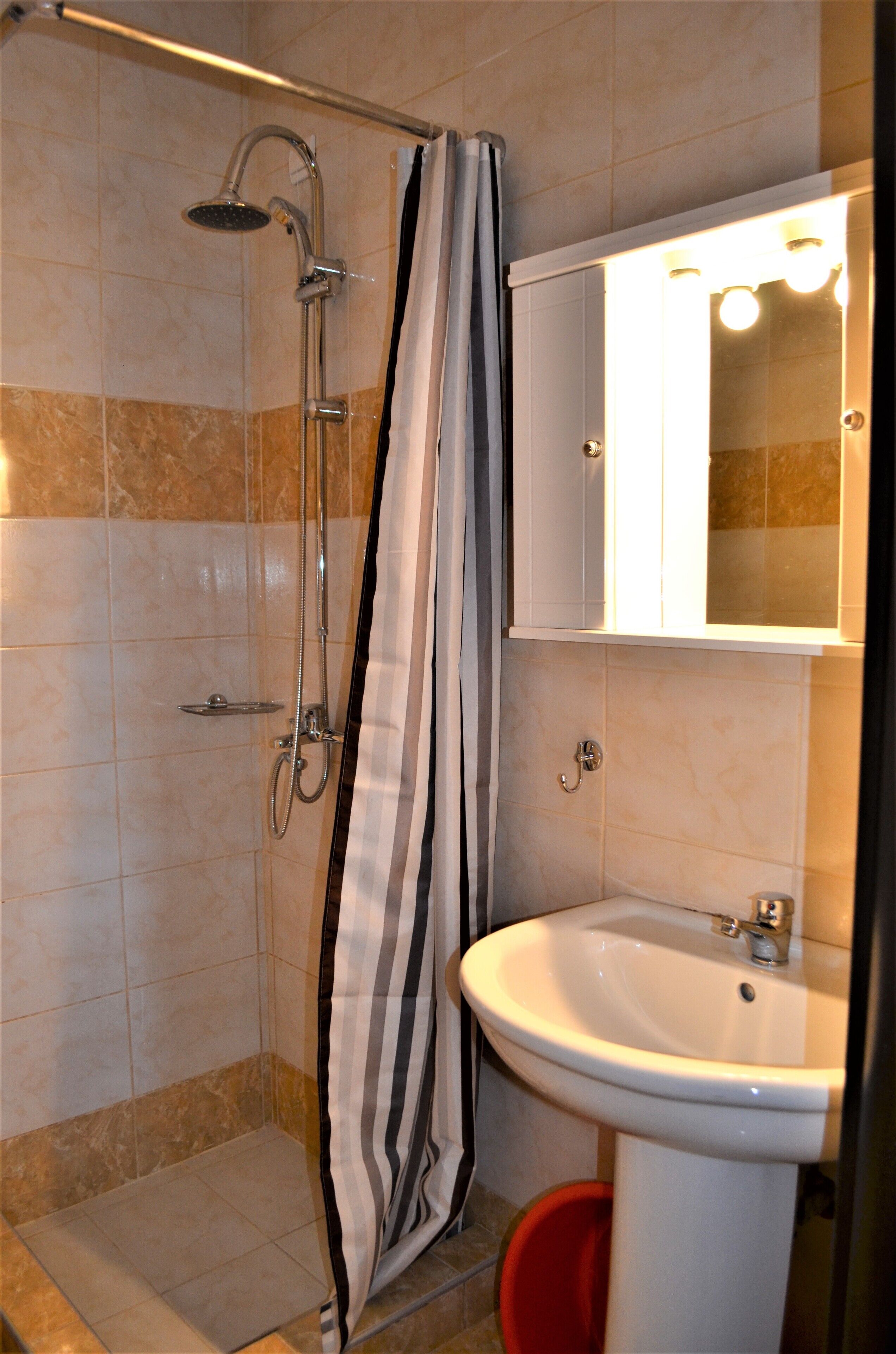 A bathroom with a shower, a sink, and a mirror with lights.