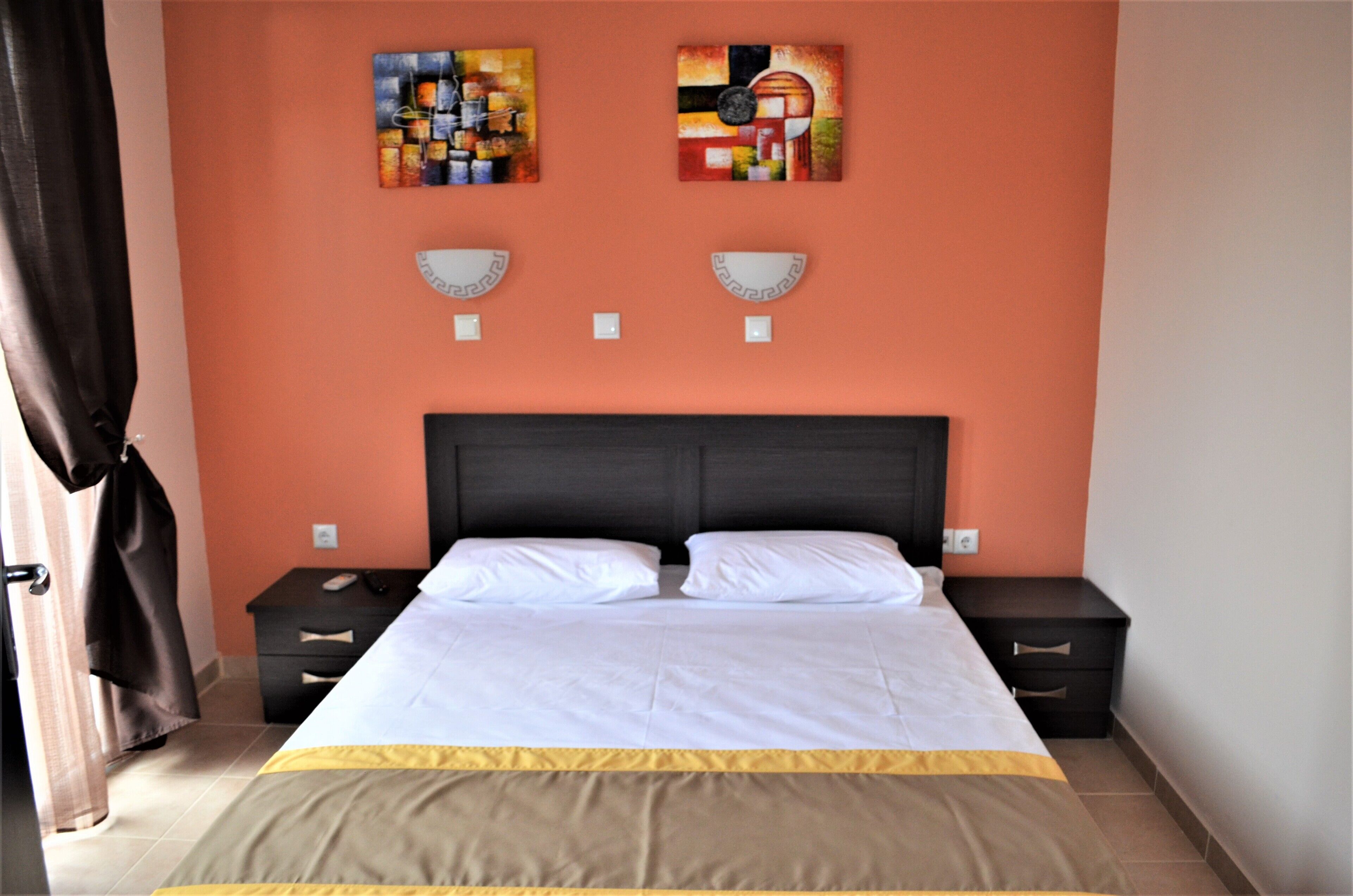 A bedroom with a large bed, two bedside tables, a dark headboard, and two abstract paintings on the wall.