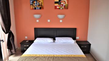 A bedroom with a large bed, two bedside tables, a dark headboard, and two abstract paintings on the wall.