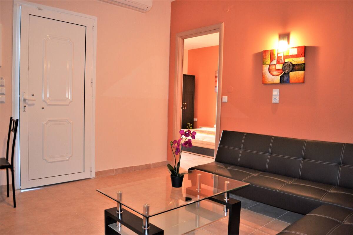 A modern lobby with a glass coffee table, a black leather sofa, a white door, and a wall-mounted artwork.