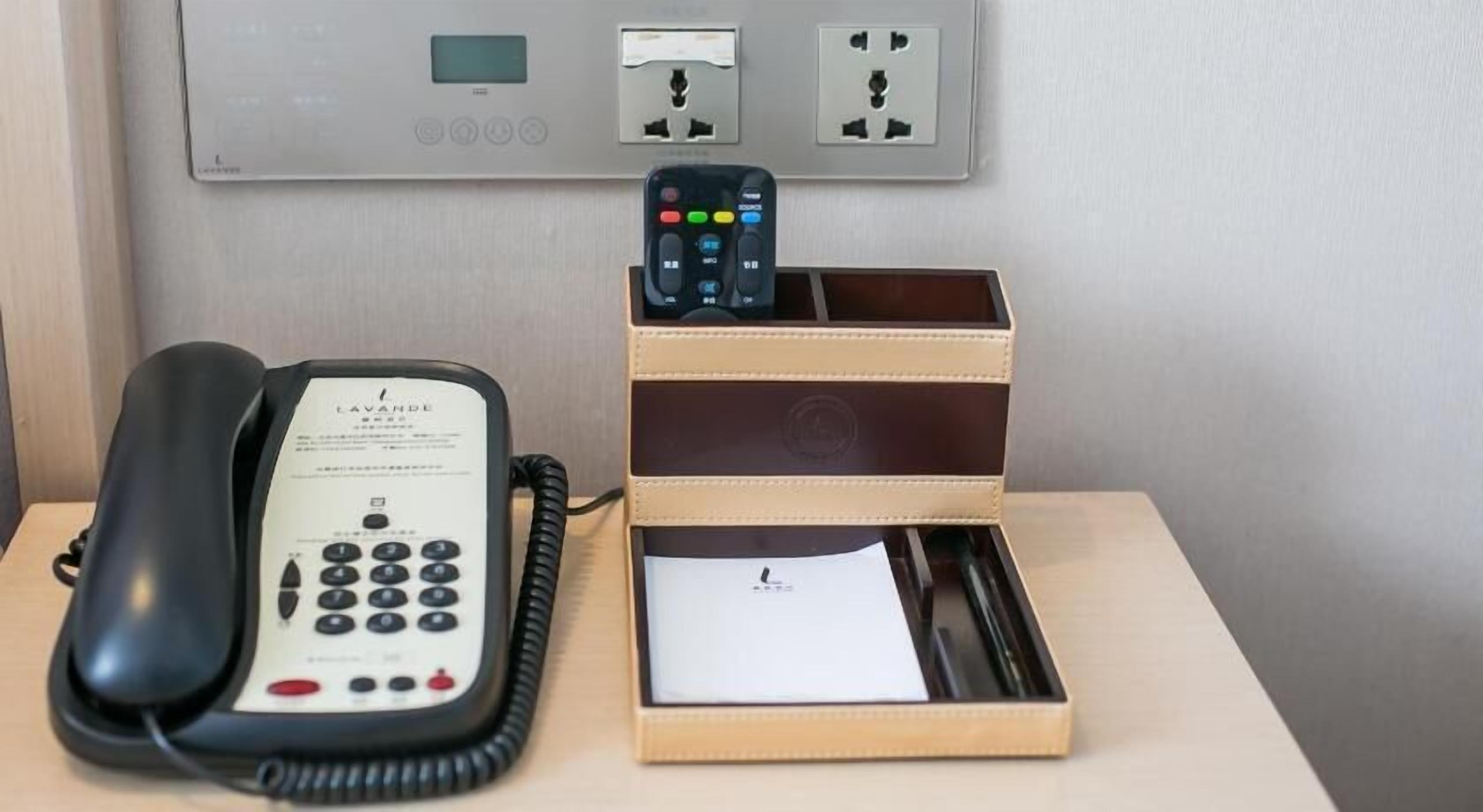 A hotel room with a telephone, a charging station, and a small wooden box with a pen and paper.