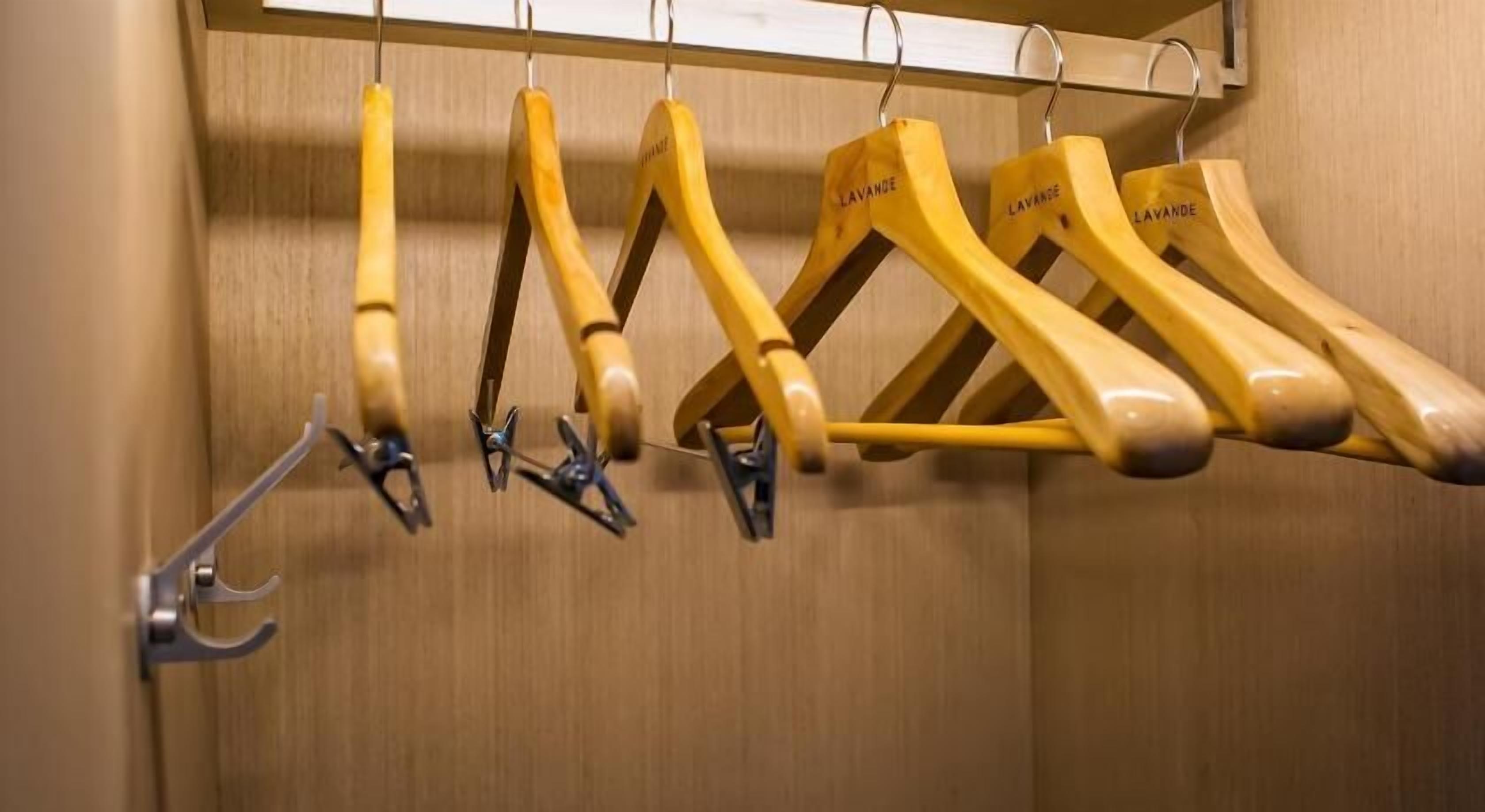 A wooden coat rack with multiple hangers, some with metal clips.
