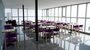 Une pièce spacieuse avec de grandes fenêtres, plusieurs tables et des chaises violettes, ainsi qu'un plancher ciré.
