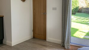Una habitación con puerta de madera, un adorno en forma de corazón en la pared, una cortina estampada y vistas de un jardín a través de una puerta de cristal.